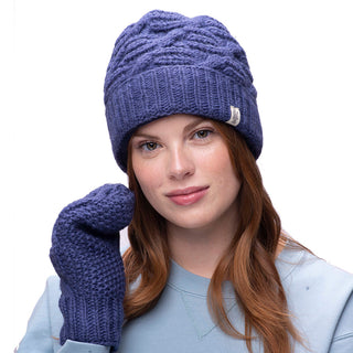 A woman wearing a blue side cable knit beanie and mittens.