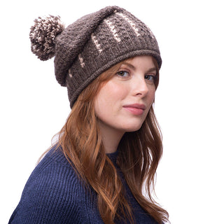 A woman with red hair wearing a brown Ferry slouch knitted beanie with a pom-pom on top.