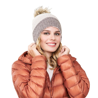 A woman in a brown puffer jacket wearing a hat with a Stripe flower fur pom pom.
