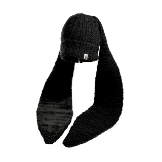 The Oversized Ear Beanie, a black knit winter hat, features two long flaps extending from the sides, likely intended to hang down over the ears for warmth. The design is simple yet functional.