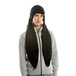 A person stands wearing a gray zip-up hoodie and the Oversized Ear Beanie, a knitted dark gray hat with long, scarf-like extensions hanging down on each side. The background is plain black. The individual has a neutral expression.