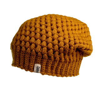 A mustard yellow Bubble Hat showcases a honeycomb pattern, complete with a ribbed brim and a small white tag featuring an illustration of two trees on the bottom edge. The background is transparent.