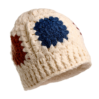 The Crochet Patch Hat, a white, knitted beanie adorned with large, round crocheted patches in blue, red, and brown, is showcased. The hat boasts a textured, ribbed design and is positioned with a slight tilt to the right.