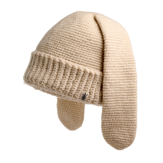 The Rib EarPup Hat is a beige knitted cap with two long ear-flap extensions hanging down. It features a ribbed pattern around the brim and a small tag with a tree logo on the side. The background is white.