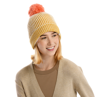 A woman with light hair wearing a beige sweater and an Allen Pom Hat, made from Merino Wool and showcasing a yellow-and-white knit design topped with a pink pom-pom, smiles as she looks to the side, standing against a plain black background.