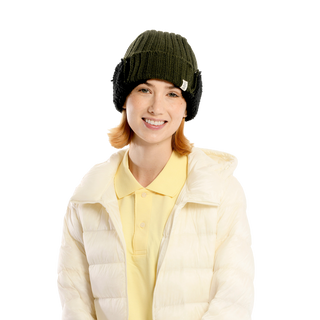 A person is wearing a yellow polo shirt under a white puffer jacket. They have the Astor Hat in green, complemented by black earmuffs, adding a cozy touch. The background is plain and black.