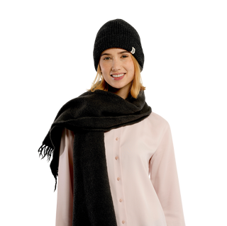 A person wearing a light pink blouse, the Bond Hat in black knit, and a long black scarf is smiling against a plain black background.