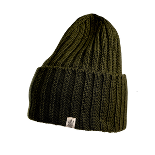 The Cooper Hat is an olive green knitted beanie featuring a ribbed pattern and a folded cuff, meticulously crafted from premium merino wool. This stylish outdoor headwear also includes a small white tag with a logo attached to the cuff.