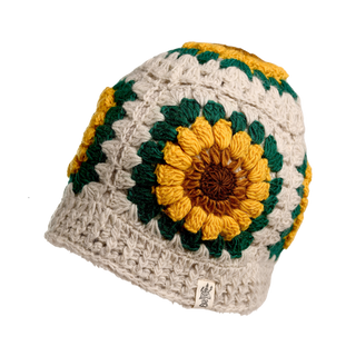 Presenting the Sunflower Sun Hat, a hand-crocheted beanie adorned with a sunflower design. The hat predominantly features a beige color, accented by green, yellow, and brown yarn that forms a large sunflower pattern on the side. A small tag with a logo is attached to the hem for added detail.