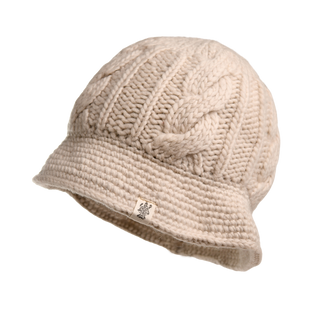 The Nostrand Hat, a beige cable knit accessory made from luxurious merino wool, boasts a softly draped wide brim and a small fabric tag bearing an inscribed logo near the base. Ideal for your winter wardrobe, the hat is showcased against a plain white background.