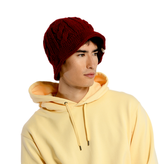 A person is looking off to the side while donning a red Nostrand Hat and a light yellow hoodie. The backdrop is plain and the lighting is even, highlighting the vibrant colors of their winter wardrobe.