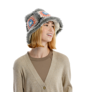 A person with shoulder-length blonde hair is wearing a beige cardigan over a brown top, perfectly suited for cold-weather fashion. They have on a Crochet Sun Hat With Fur Piping, featuring colorful crocheted squares and faux fur piping in gray. The person is looking to the side and smiling.