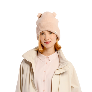 A person wearing a light pink Bear Cub Ears Hat made from cozy merino wool, paired with a pale pink button-up shirt and an off-white jacket, stands against a plain black background.