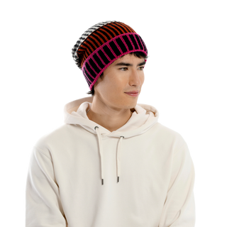 A person with short dark hair is wearing a white hoodie and the Atlantic Hat, a colorful, hand-knit Merino wool beanie featuring a mix of black, red, orange, and pink stripes. The person is looking to the right against a plain black background.