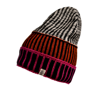 The Atlantic Hat is a hand-knit Merino Wool beanie that showcases a multicolor, multi-patterned knit design. It features a black and white houndstooth pattern on top, red and black vertical stripes around the middle, and is finished with a pink and black border at the bottom. The hat also includes a visible tag.