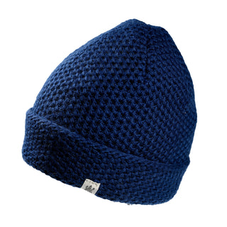 Hand Knit Baltic Hat in dark blue wool with a folded cuff and a small woven tag featuring a crest logo.