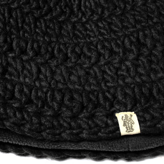 Close-up of the textured black fleece lining from the Hand Crochet Acorn Hat, featuring a small off-white tag sewn into the edge. The tag displays a detailed line drawing of a person in traditional attire.