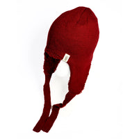 A mannequin head displays the Hand Knit Snug Hat, a warm red winter hat with long ear flaps and ties. This hand-knit earflap hat showcases a textured pattern and is accented with a small beige label on the side. The background is plain white.