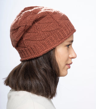 A woman with shoulder-length brown hair is shown in profile wearing the Wave Slouch, a textured rust-colored beanie, and a light-colored top against a white background.