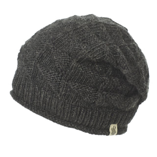 The Hand Knit Wave Slouch is a dark gray hand loom knit beanie with a ribbed brim, textured pattern, and small fabric tag on the brim, displayed against a white background.