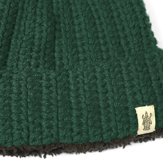 Close-up of the Hand Crochet Chunky Hat in green lambswool, showcasing a brown inner lining and a small beige fabric tag with a printed logo near the bottom edge.