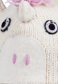 Close-up of a cream-colored Hand Knit Unicorn Hat from Nepal featuring a central horn, pink yarn mane, embroidered eyes, and a felt snout with pink stitched nostrils.