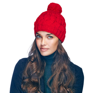 A woman with long wavy hair wearing a red Dante Beanie with Pom, handmade in Nepal, and a dark turtleneck sweater.