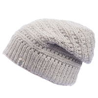Introducing the Hand Knit Boho Slouch—a light gray handmade wool beanie featuring a ribbed band and a small fabric tag on the side. This hat boasts a slouchy style and showcases a textured pattern throughout the knit.