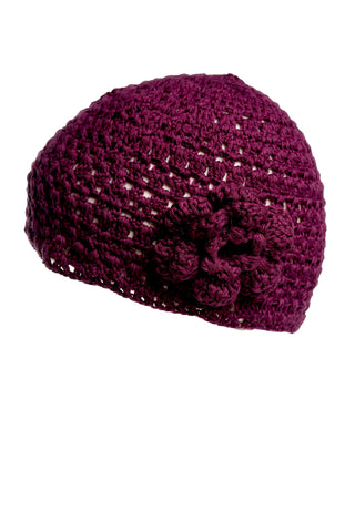 A close-up image of the Flower Beanie, a purple knit hat adorned with a hand-crocheted flower detail on the side. The hat showcases a textured, open weave pattern. As part of our summer collection, it pops beautifully against the plain white background.