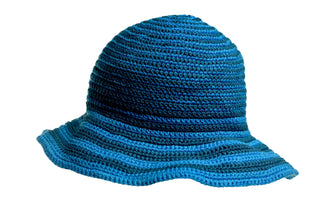 The Stripped Sun Hat, a blue crocheted sun hat with a wide, slightly wavy brim, is displayed against a white background. This stylish hat features alternating light and dark blue horizontal stripes.