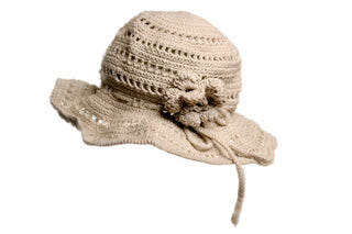 The Flower Sun Hat is a beige crocheted accessory featuring a wide, slightly floppy brim and a decorative flower on one side. It boasts intricate stitching patterns throughout and is displayed against a plain black background.