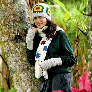 A person wearing the handmade wool Sunflower Hat stands by a tree in a lush outdoor setting, smiling at the camera and showing off this cozy winter accessory.