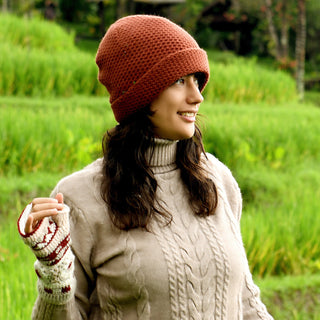 A person wearing the Baltic Hat—a cozy, handmade brown wool hat from Nepal—stands outdoors in a green field, smiling and looking to the side.