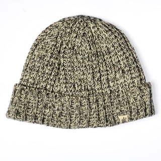 The Hand Knit Grid hat is showcased against a plain white background, featuring a marled pattern in cream and gray yarn, a folded brim, and a small fabric tag on the edge.
