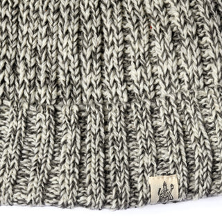 Close-up of a gray and white knitted fabric from the Hand Knit Grid hat, featuring a small beige tag with a black illustrated design attached at the seam.