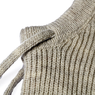 Close-up of the Hand Knit Cozy Hood in beige wool, featuring a ribbed texture with a visible shoulder seam and a narrow knitted strap, set against a white background.