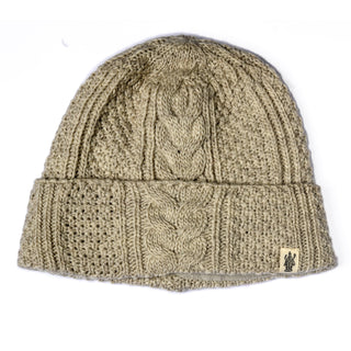 The Hand Knit Inter Hat is a beige cable knit beanie featuring a classic cable-knit pattern and a folded brim. A small rectangular fabric tag with the logo is sewn onto the brim, adding a subtle accent to this cozy winter essential.