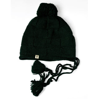 The Hand Knit Nest Hat is a dark green, wool hat with ear flaps, braided tassels, and playful pom-poms at the ends. Lined with soft sherpa for added warmth, this handmade Nepal hat also features a larger pom-pom on top and a small metallic tag on the brim. The hat is shown laid flat on a white background.