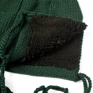 A close-up of the Hand Knit Nest Hat in green, featuring a hand knit wool exterior and a plush, black sherpa lining inside—highlighting the detailed textures of both the cozy knit surface and the soft interior that make this earflap hat extra warm.