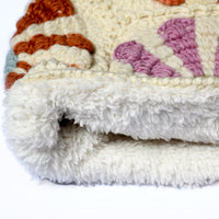 A close-up of the edge of the Hand Crochet Petal Hood, featuring a white, fluffy base with a textured, colorful pattern reminiscent of crochet daisies. The image highlights its thickness and soft pile against a plain background.