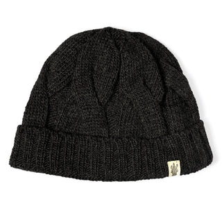 The Hand Knit Nord Hat is a black wool beanie with a folded brim and a small beige logo tag on the side. This cuffed, hand-knit hat is shown against a white background.