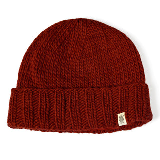 A Hand Knit Timber Hat in red wool, featuring a folded brim and a small beige tag with a simple graphic, shown laying flat on a white background.
