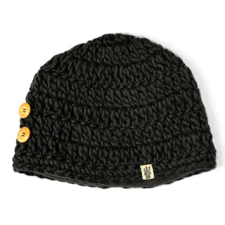 The Hand Crochet Acorn Hat is a black knitted beanie with a textured pattern, featuring two wooden buttons on one side and a small fabric tag with a logo. This soft wool winter beanie blends classic style with cozy warmth—perfect for chilly days.