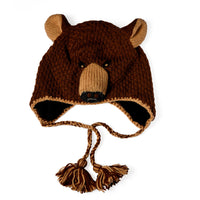 The Hand Crochet Grizzly Hat is a wool hat handcrafted to resemble a bear’s face, complete with round ears, a snout, black eyes, and braided tassels hanging from each side. It is displayed on a white background in the photograph.