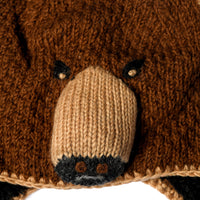 Close-up of the Hand Crochet Grizzly Hat featuring a knitted brown and beige bear face with black embroidered eyes and nose, detailed stitching and texture, and a soft sherpa lining for added warmth—perfect for cozy wear.
