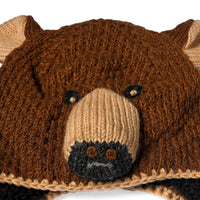 Close-up of the Hand Crochet Grizzly Hat, a wool accessory crafted to resemble a bear’s face, featuring brown and beige yarn, black crocheted eyes, a protruding snout, small rounded ears, and cozy sherpa lining for added warmth.