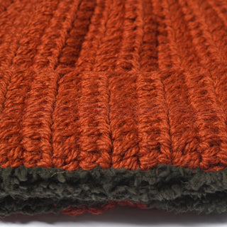 Close-up of a thick, ribbed knit fabric in rust orange on top and dark gray on the bottom, showing texture and fibers of the yarn. The image highlights the stitching detail and contrast between the two colors, capturing the warmth and craftsmanship of the Hand Crochet Chunky Hat.