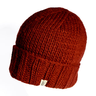 A close-up of the Hand Knit Timber Hat, a thick, hand-knitted red-brown wool docker-style beanie featuring a folded brim and a small beige tag, set against a white background.