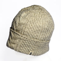 A classic beige Hand Knit Inter hat featuring a timeless cable knit pattern is displayed on a white mannequin head. A small fabric tag accents the brim near the bottom edge, while the plain white background highlights this hand knit wool beanie.