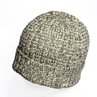 A close-up of the Hand Knit Grid hat, a gray and white beanie with a cuffed edge, displayed on a white background. This handmade hat showcases a ribbed texture and features a small sewn tag near the bottom edge.